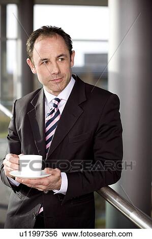 Businessman in office drinking a cup of coffee View Large Photo Image Stock Photograph - Businessman in office drinking a cup of coffee. Fotosearch