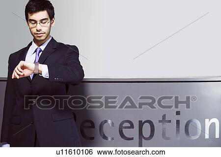 Stock Photograph - Businessman waiting at office reception, looking at his watch. Fotosearch