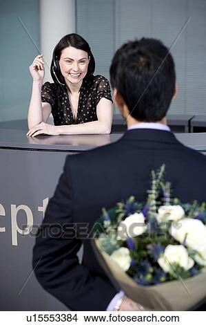 Businessman with bouquet of flowers being greeted by office receptionist View Large Photo Image Picture - Businessman with bouquet of flowers being greeted by office receptionist. Fotosearch