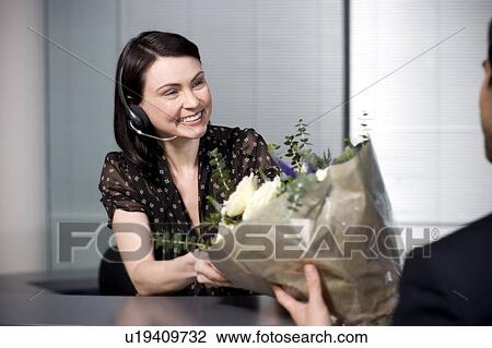 Stock Image - Businessman with bouquet of flowers being greeted by office receptionist. Fotosearch