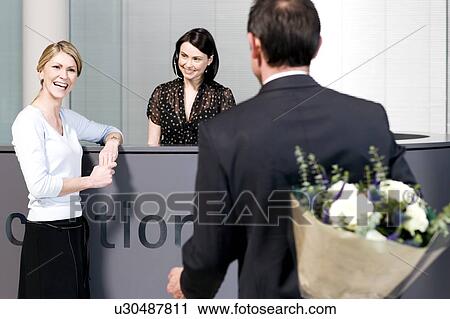 Businessman with bouquet of flowers being greeted by two women at office reception View Large Photo Image Stock Image - Businessman with bouquet of flowers being greeted by two women at office reception. Fotosearch