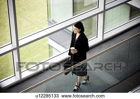 Stock Image - Businesswoman in modern office building, arriving for work. Fotosearch