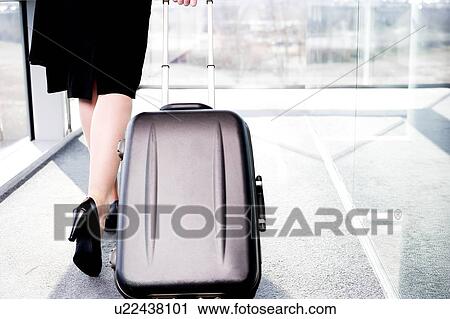 Stock Image - Businesswoman traveling, pulling suitcase along inside station or airport. Fotosearch
