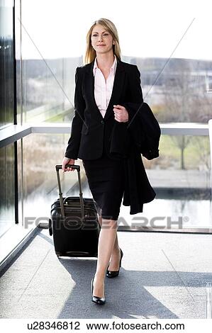 Stock Image - Businesswoman traveling, pulling suitcase along inside station or airport. Fotosearch
