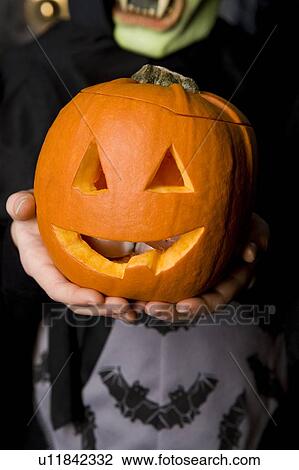 Stock Image - Child holding Hallowe'en pumpkin with a carved face. Fotosearch
