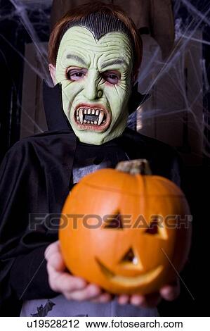 Stock Image - Child in a Count Dracula costume at Hallowe'en, holding a pumpkin with a carved face. Fotosearch