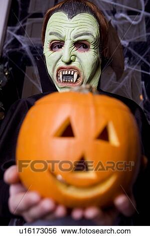 Stock Photograph - Child in a Count Dracula costume at Hallowe'en, holding a pumpkin with a carved face. Fotosearch