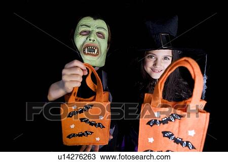 Stock Image - Children in costumes at a Hallowe'en party, holding orange party bags. Fotosearch