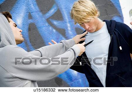 Stock Image - Confrontation between two young men and a group of friends in front of a graffiti covered wall . Fotosearch