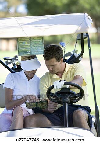 Stock Photograph - Couple in a golf buggy looking at a plan of the course and score card. Fotosearch
