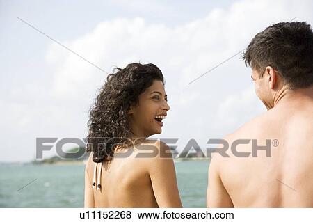 Stock Photo - Couple sitting beside the sea on a summer holiday. Fotosearch