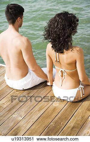 Couple sitting on the side of a wooden jetty by the sea, holding hands View Large Photo Image Stock Image - Couple sitting on the side of a wooden jetty by the sea, holding hands. Fotosearch