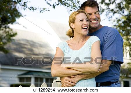 Picture - Couple standing by the garden fence outside their new home. Fotosearch