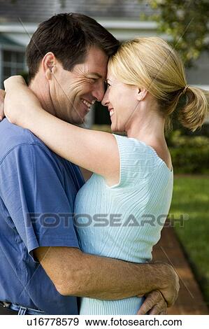 Stock Photo - Couple standing on the garden path outside their new home, hugging. Fotosearch