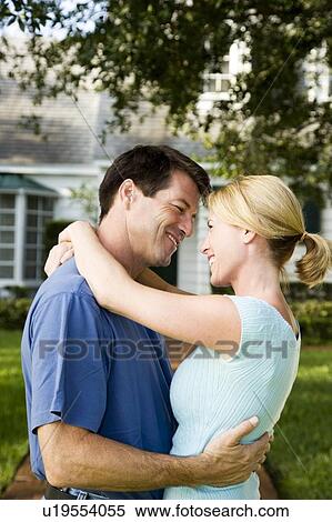 Stock Photography - Couple standing on the garden path outside their new home, hugging. Fotosearch