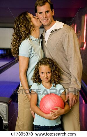Stock Photo - Family in a bowling alley, daughter holding a red bowling ball. Fotosearch