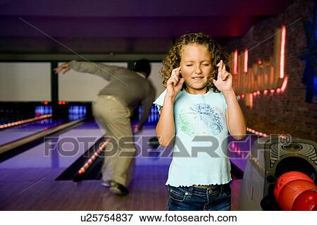 Stock Photo - Father and daughter bowling, daughter crossing her fingers for good luck. Fotosearch