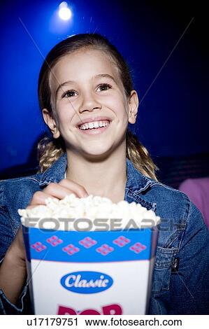 Stock Image - Girl eating popcorn at the cinema. Fotosearch