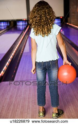 Stock Photo - Girl in a bowling alley holding a red bowling ball. Fotosearch