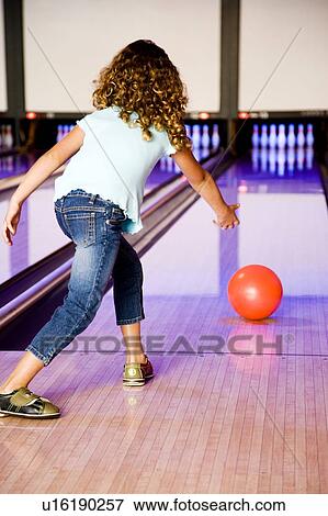 Stock Photo - Girl in a bowling alley rolling a red bowling ball. Fotosearch