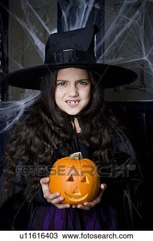 Stock Image - Girl in a witch's costume at a Hallowe'en party, holding a pumpkin . Fotosearch