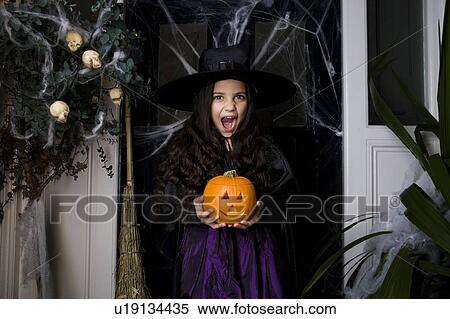 Stock Photography - Girl in a witch's costume at a Hallowe'en party, holding a pumpkin . Fotosearch