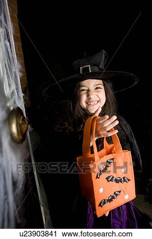 Stock Image - Girl in costume at a Hallowe'en party, holding an orange party bag. Fotosearch