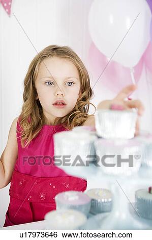 Stock Photograph - girl in taking cake from cake stand at birthday party. Fotosearch