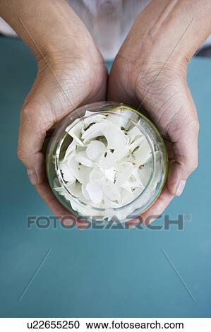 Stock Image - Hands holding small glass pot of white flowers. Fotosearch