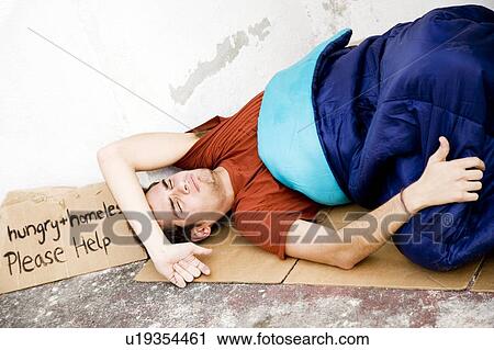 Stock Image - Homeless young man laying in the street . Fotosearch