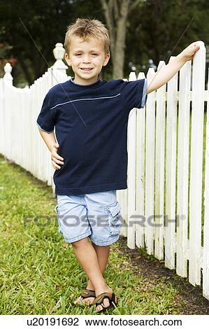 Stock Image - little boy standing by picket fence. Fotosearch