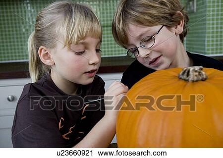 Stock Image - Little girl and boy making a pumpkin lantern. . Fotosearch