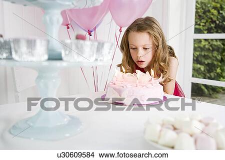 Picture - little girl blowing out candles on birthday cake. Fotosearch