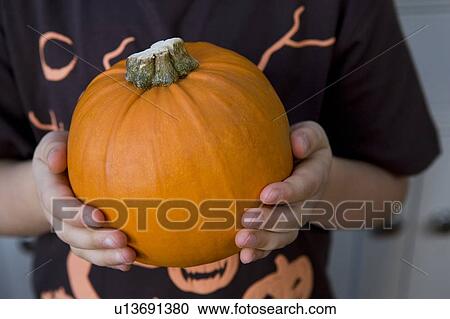 Stock Image - Little girl holding an orange Hallowe'en pumpkin. Fotosearch