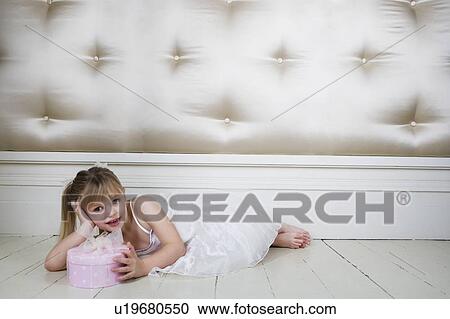 Stock Image - Little girl in a party dress, laying on the floor with a present. Fotosearch