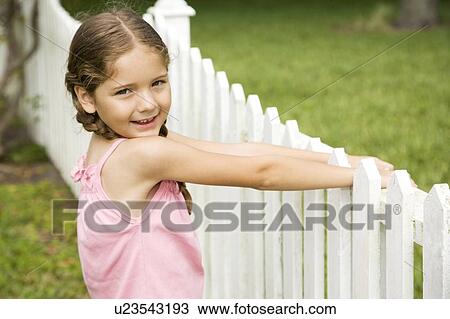 Stock Image - little girl standing by picket fence. Fotosearch