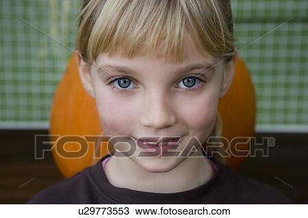 Stock Image - Little girl standing in front of an orange Hallowe'en pumpkin. Fotosearch