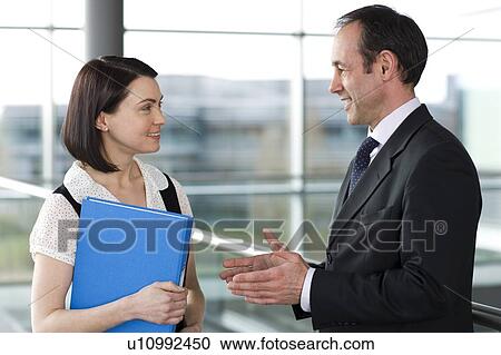 Stock Image - Male and female business colleagues chatting in office building. Fotosearch