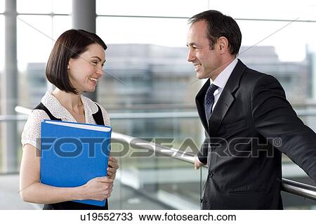 Stock Image - Male and female business colleagues chatting in office building. Fotosearch
