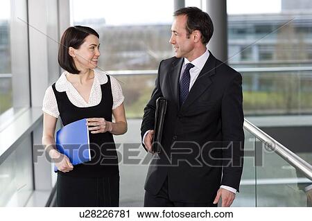 Stock Image - Male and female business colleagues chatting in office building. Fotosearch