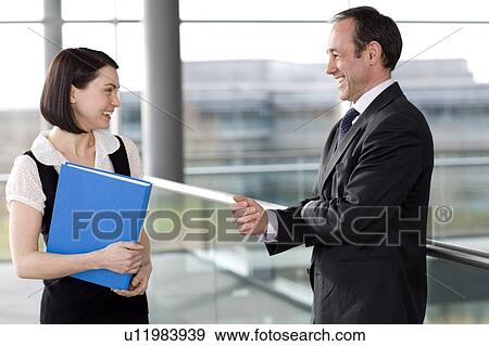 Stock Photo - Male and female business colleagues chatting in office building. Fotosearch