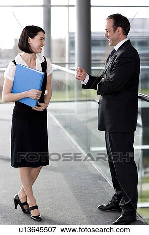 Male and female business colleagues chatting in office building View Large Photo Image Stock Photo - Male and female business colleagues chatting in office building. Fotosearch