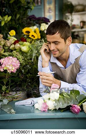 Stock Image - Male florist at the shop counter, taking an order over the telephone. Fotosearch