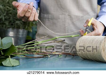 Picture - Male florist creating a bouquet of flowers, cutting the twine. Fotosearch