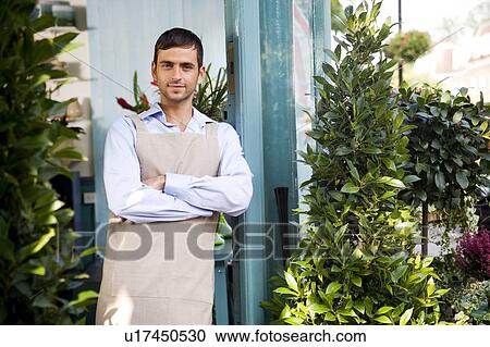 Stock Image - Male florist standing at the entrance to his shop. Fotosearch
