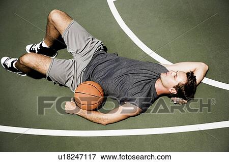 Stock Photo - Man laying down on an outdoor basketball court . Fotosearch