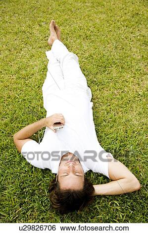 Stock Photograph - Man lying on the grass listening to personal stereo. Fotosearch