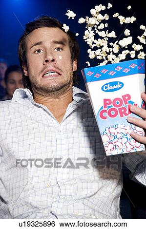 Stock Photograph - Man reacting to a film at the cinema, popcorn flying. Fotosearch