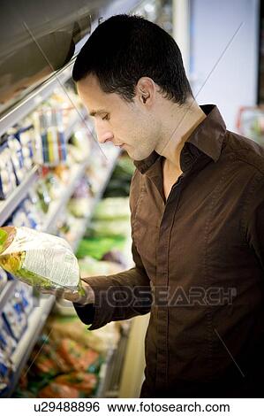 Stock Photograph - Man reading the label on food packaging in a supermarket. Fotosearch