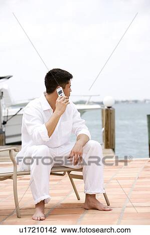 Man sitting by a boat in the harbour, talking on a mobile phone View Large Photo Image Stock Image - Man sitting by a boat in the harbour, talking on a mobile phone. Fotosearch
